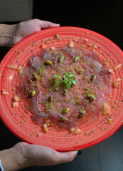 Hands Holding Plate of Mediterranean Tuna Carpaccio