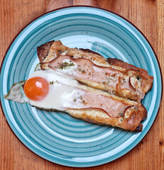 Turquoise plate with toasted bread topped with ham, cheese, and a sunny-side-up egg