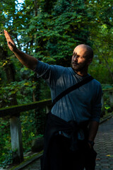 Man in a forested area, extending his arm toward the sunlight filtering through the trees, creating a dramatic shadow.