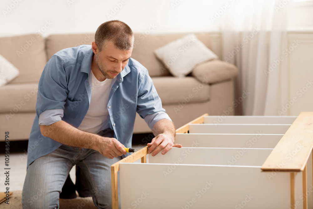 Poster middle-aged male installing wooden cabinet using screwdriver at home. man furnishing house assemblin