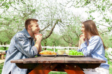 young couple in love in denim clothes sitting in the garden at a wooden table and talking in the summer, guy and girl on a date talking and flirting in the park