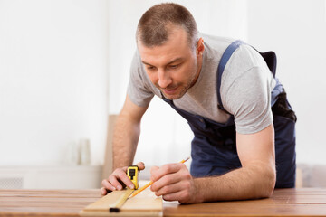 Carpentry Concept. Professional Carpenter Measuring Wooden Board Working On A Piece Of Furniture Indoors. Selective Focus