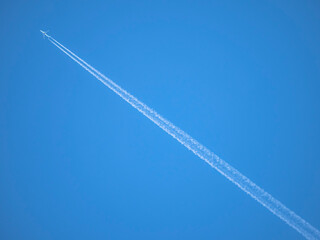 White streaks of planes leave behind like artificial clouds crossing the image diagonally across the photograph on a blue sky background