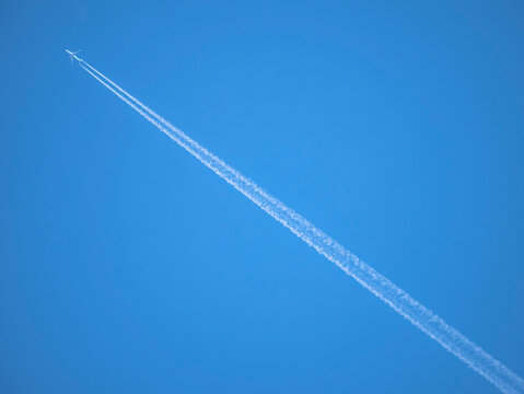 White streaks of planes leave behind like artificial clouds crossing the image diagonally across the photograph on a blue sky background