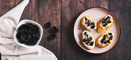 Homemade bruschetta with cream cheese and prunes on a plate top view web banner