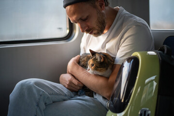 Man traveling on train with beloved cat sitting calmly on lap. Male pet owner enjoys peaceful electric train journey with fluffy cat. Comfortable trip with feline companion in public transportation