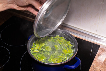 man's hand uncovering a pot containing cut green flat beans in boiling water