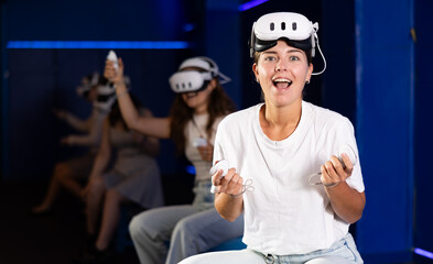 Girl gamer with virtual reality glasses on her forehead expresses enthusiastic emotions from...