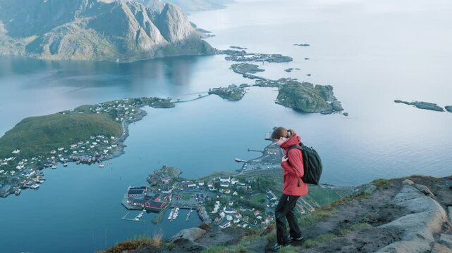Young girl in red jacket walks on top of mountain admiring beautiful view of Norwegian sea, Reinebringen
