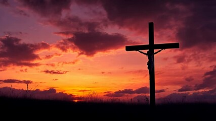 A silhouette of a crucifix stands tall against a vibrant sunset sky