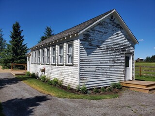 Old school building in the country side now used as a museum. White in color with old shiplap siding and many windows.