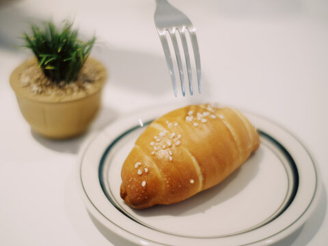A croissant in a saucer with a silver fork and decorative plant