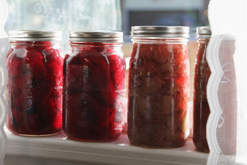 Homemade canned beets and rhubarb on a window sill; colorful display of old-fashioned food preserves
