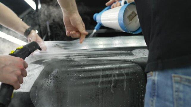 Professional car detailers apply a protective film to a vehicle's hood, ensuring a clean and shiny surface