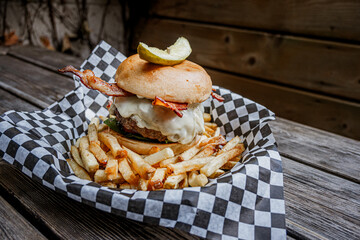 Cheese Burger with bacon and pickle on top over french fries on patio table