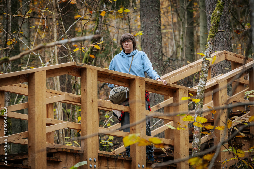 Wall mural a person wearing a light blue hoodie stands on a wooden bridge surrounded by an autumn forest. the l