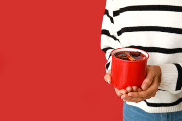 Young woman with cup of hot mulled wine on red background