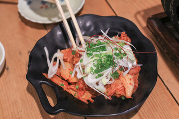 Stir-fried pork with kimchi and vegetables in black plate. Korean food style.