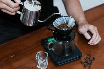 Closeup of a hand making a drip coffee or v60 method, pouring hot water from kettle over a ground coffee powder in the funnel, making coffee homemade.