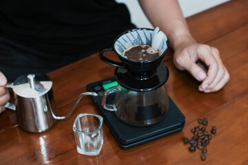 Closeup of a hand making a drip coffee or v60 method, pouring hot water from kettle over a ground coffee powder in the funnel, making coffee homemade.