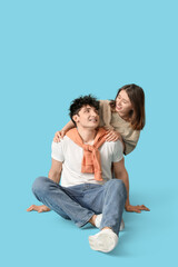 Fototapeta premium Young beautiful couple in stylish clothes sitting on floor on blue background
