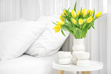 Vase of yellow tulips near bed in bedroom