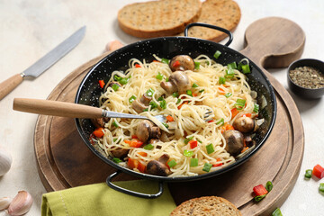 Frying pan with tasty pasta, mushrooms and bread on light background