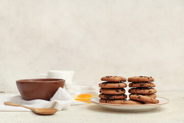 Plate of sweet cookies with chocolate chips and ingredients on white background