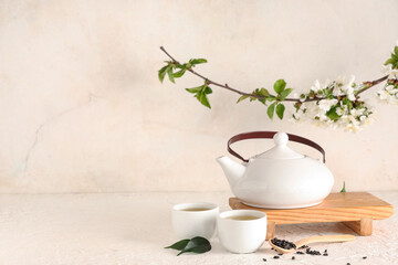 Wooden stand with teapot, cups, spoon of dry tea and leaves on light background