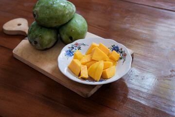 Peeled mango slices on a white plate on wooden cutting board in wooden table background, a whole ripe mango placed beside, Fresh fruit. Tropical fruit