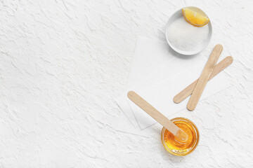 Glass bowl with sugaring paste, wax strips and wooden sticks on white background
