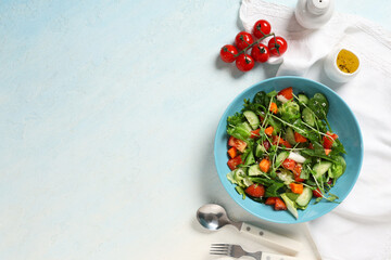 Bowl of fresh vegetable salad with tomato and cucumber on light blue background