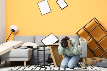 Young woman sitting on floor in living room with messed furniture after earthquake