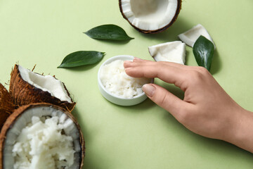 Female hand and bowl with natural coconut oil on green background, closeup