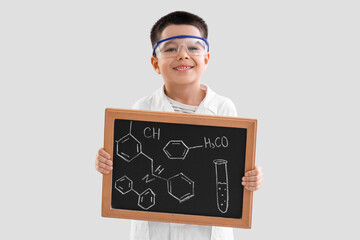 Cute little boy holding chalkboard with chemical formulas on grey background