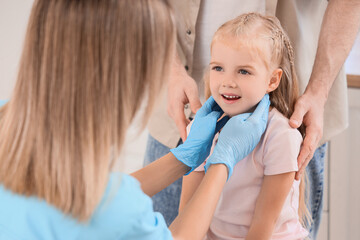 Female endocrinologist examining thyroid gland of little girl and her father in clinic