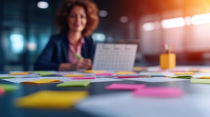 Fototapeta premium Smiling woman at desk surrounded by colorful sticky notes and a calendar.