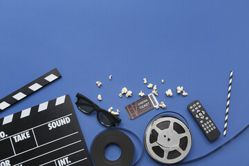 Movie clapper with remote control, cinema ticket, glasses and film reels on blue background