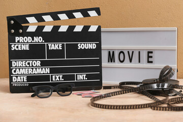 Movie clapper with word MOVIE, cinema tickets, glasses and film reels on beige table
