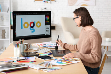 Young female designer working with graphics tablet and computer at table in office