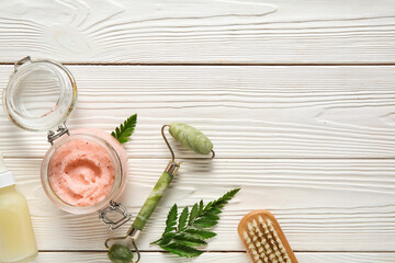 Composition with jar of natural body scrub, facial massage tool and brush on white wooden background