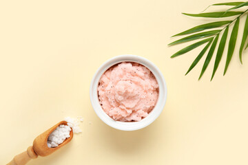 Bowl of natural body scrub, scoop with sea salt and palm leaf on color background