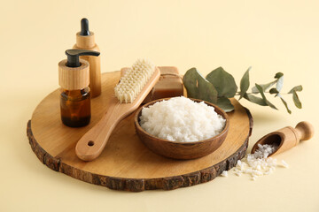 Wooden board with bowl of natural body scrub, cosmetics and massage brush on color background