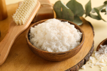 Wooden board with bowl of natural body scrub, massage brush and soap on color background, closeup