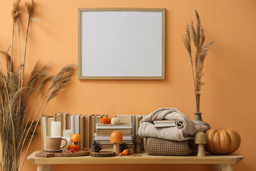 Wooden table with autumn decorations, pumpkins and books near orange wall