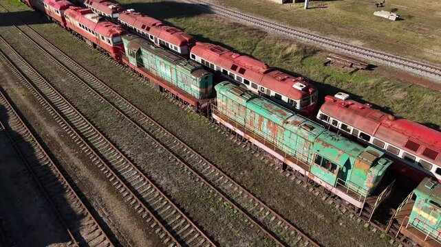 Aerial view of two diesel trains, one red and one green, connected on parallel railway tracks.