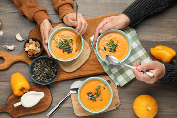 Woman and man eating delicious pumpkin soup at wooden table, top view
