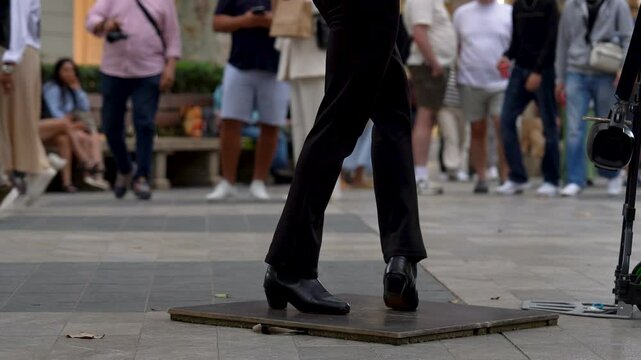 Selective Focus of Tap Dancer Legs in Barcelona while Pedestrians Walk along a Shopping Street in the Background