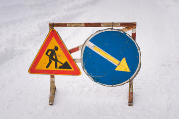 A construction warning sign and a detour sign are placed on a snow-covered road, alerting drivers...