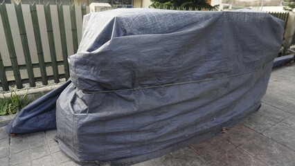 A cart covered by a tarp and tied with a rope is located on the side of the road during the day
